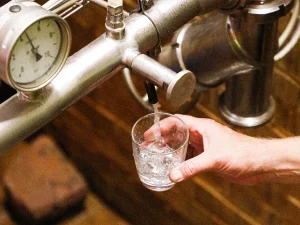 Hand hält Glas unter Edelstahl-Zapfhahn, aus dem frisches Wasser fließt
