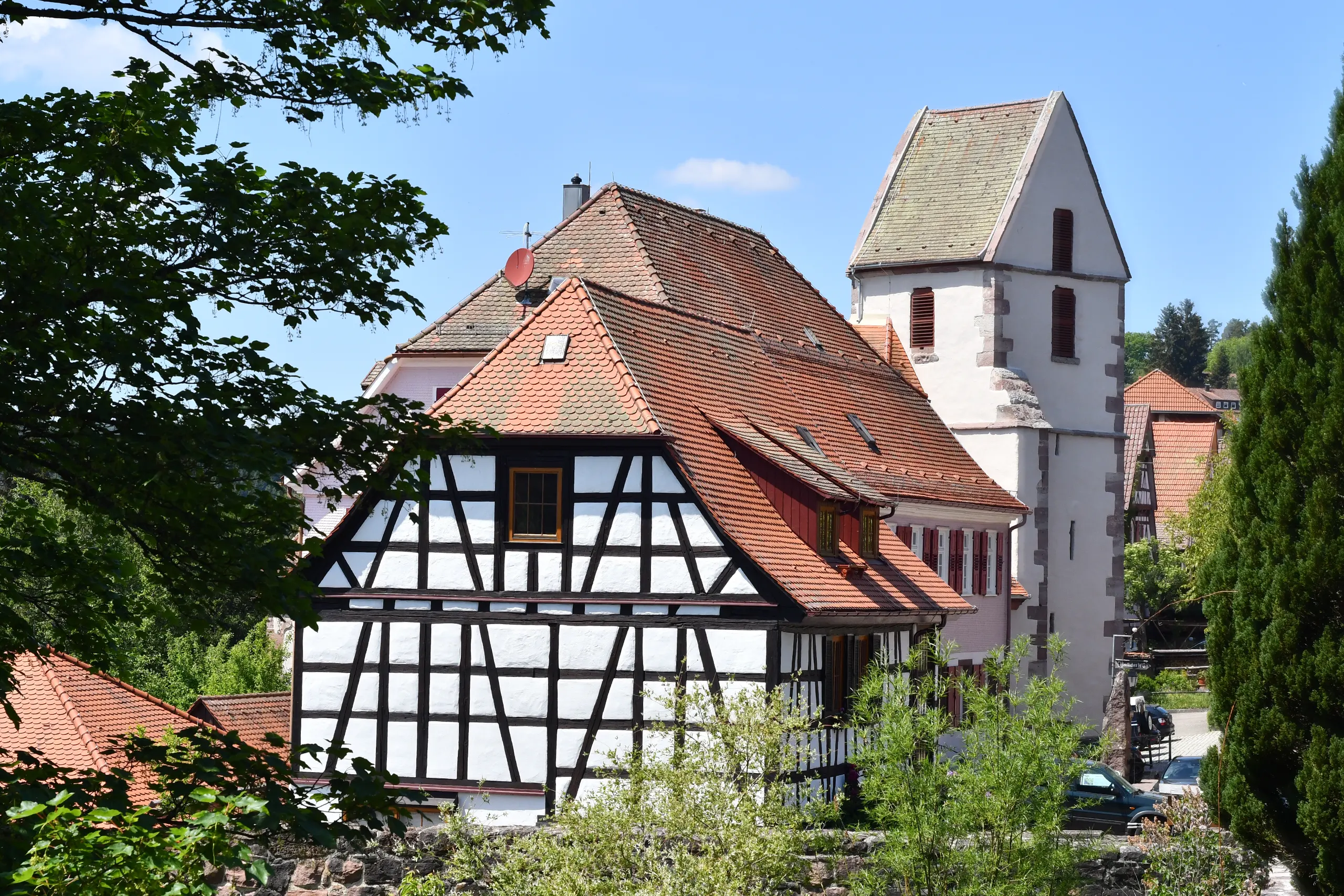 Fachwerkhaus mit rotem Ziegeldach und Kirchturm in Bad Teinach im Schwarzwald