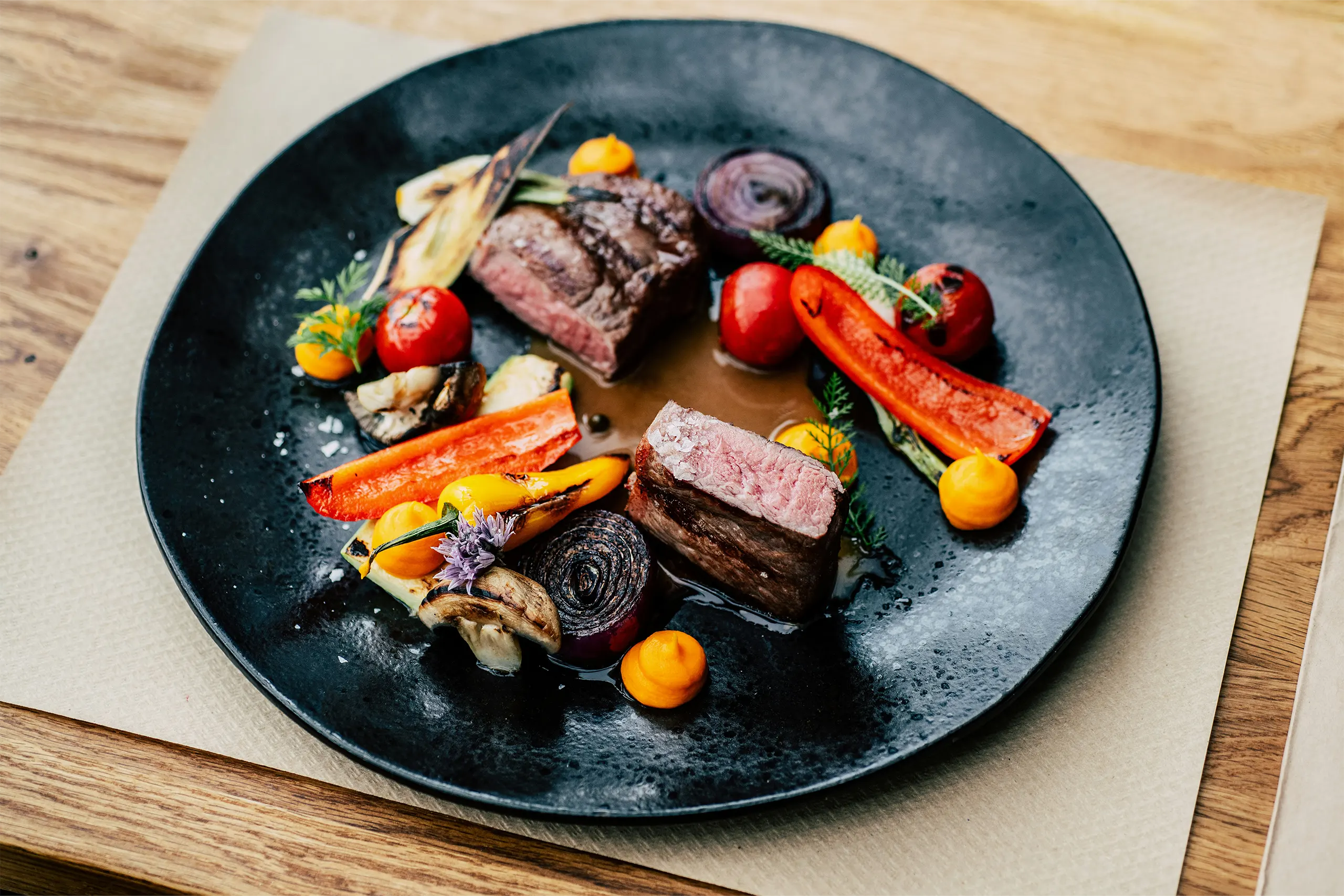 Rehfilet mit gegrilltem Gemüse und Sauce auf schwarzem Teller in einem Restaurant serviert