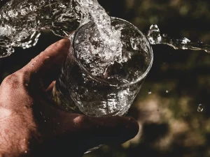 Hand hält Glas, in das sprudelndes Wasser eingegossen wird. Wassertropfen spritzen dynamisch über den Glasrand.