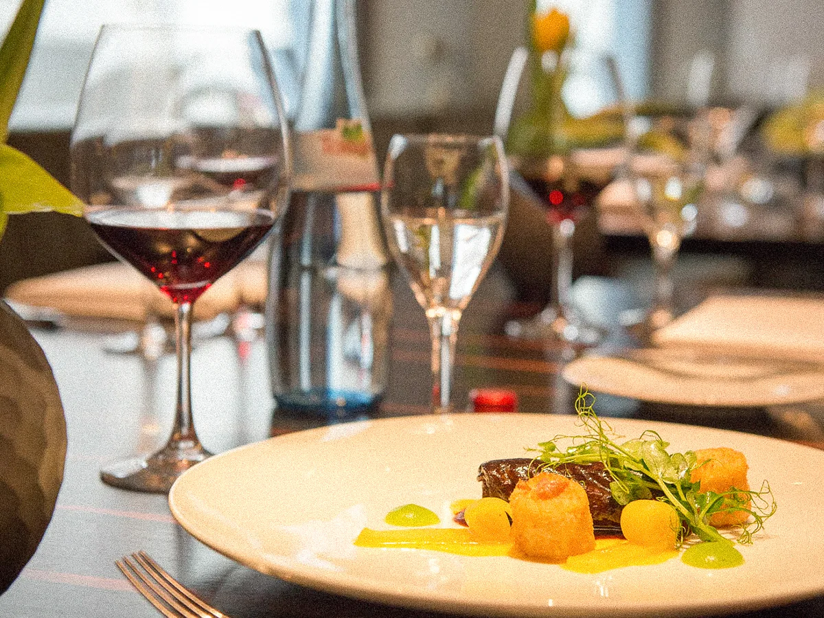 Elegant gedeckter Tisch mit Rotweingläsern, Wasserflasche und einem liebevoll angerichteten Gericht
