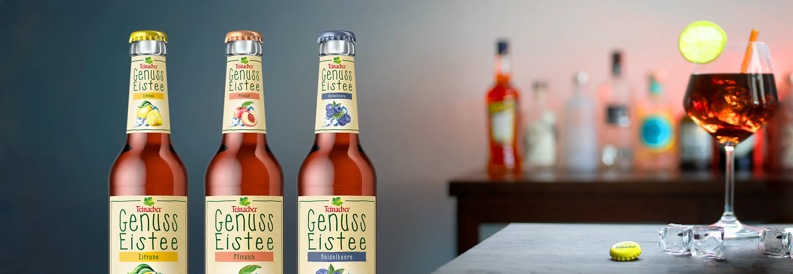 Drei Teinacher Genuss Eistee Flaschen Zitrone, Pfirsich und Heidelbeere im Vordergrund, im Hintergrund eine Bar mit Getränken und Eiswürfeln.