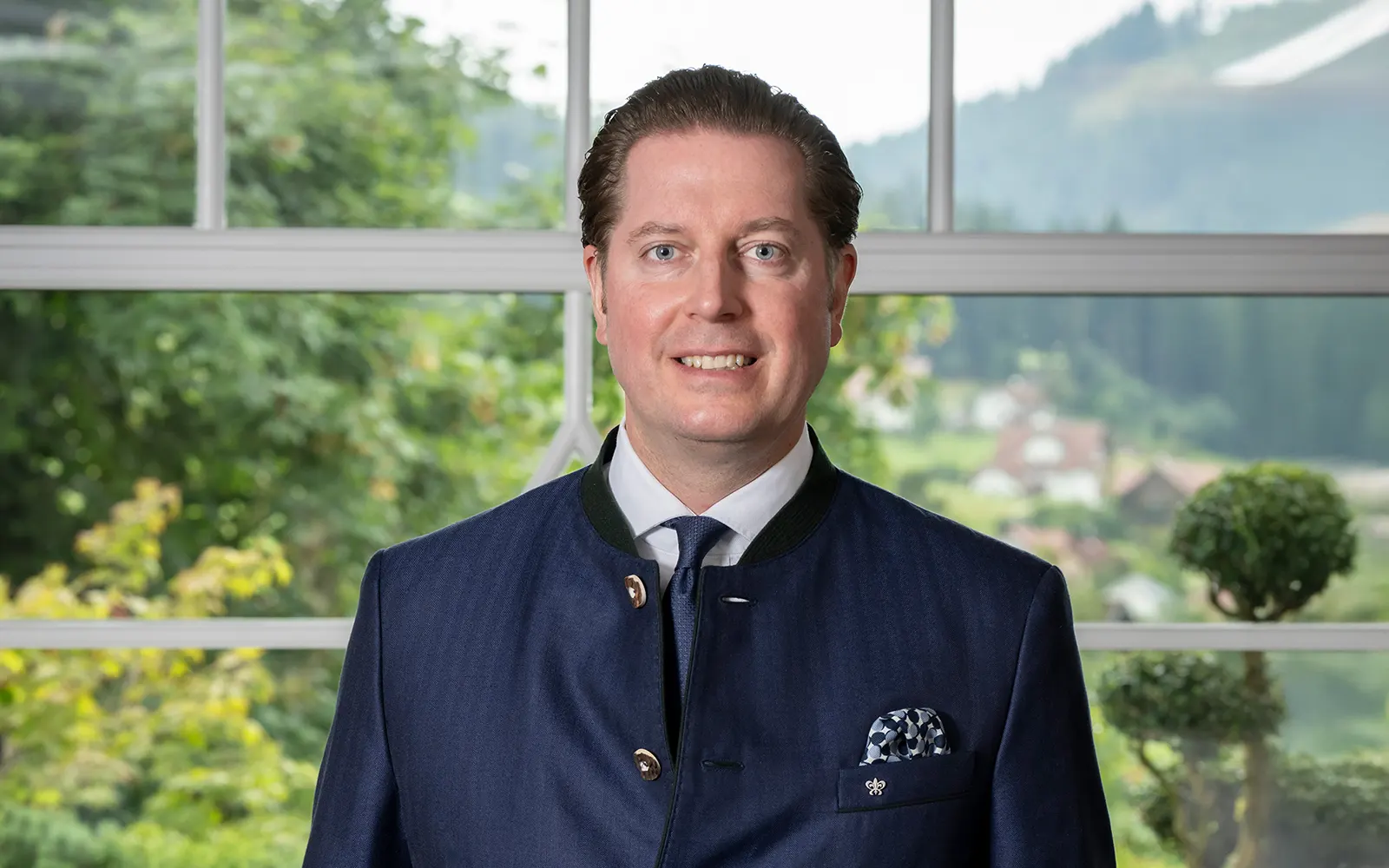 Porträt von Hannes Bareiss, Vorsitzender der FHG, vor einem Fenster mit Blick ins Grüne und eine ländliche Umgebung.