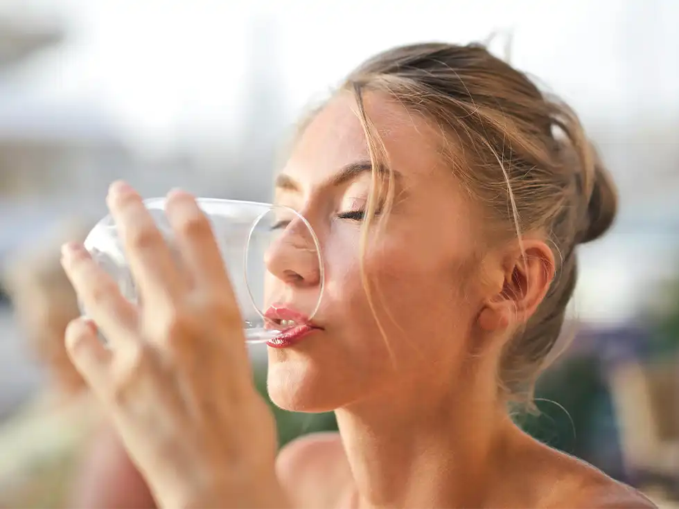 Junge Frau trinkt aus einem Glas Wasser und genießt den Moment.