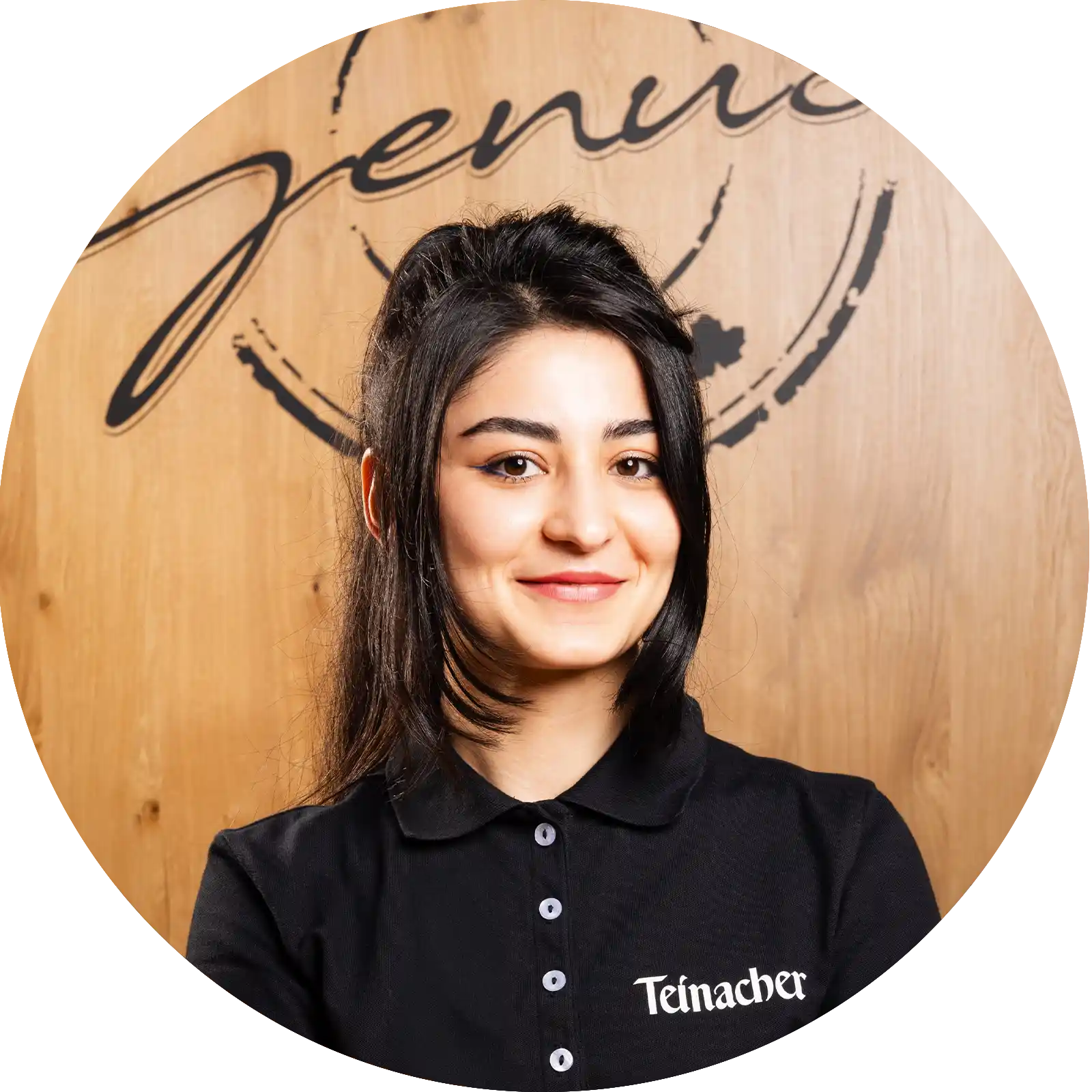 teinacher-rezepte-berry-twist-portrait-mekhron-zukurova Junge Frau in Teinacher-Shirt lächelt vor Holz-Hintergrund mit „Team Genuss“-Schriftzug.