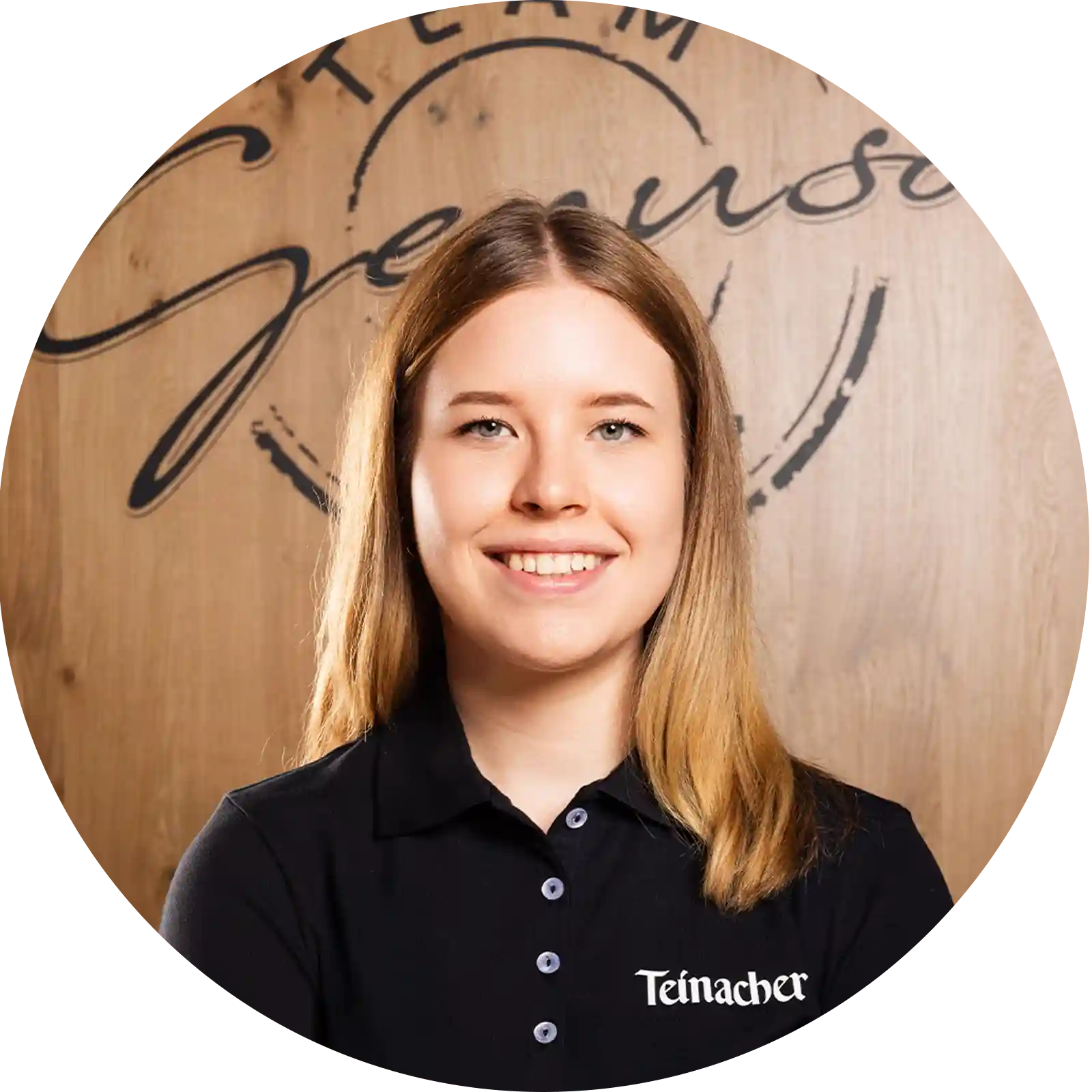 Junge Frau in Teinacher-Shirt lächelt vor Holz-Hintergrund mit „Team Genuss“-Schriftzug.