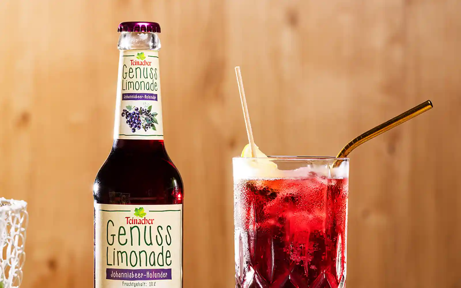 Teinacher Genusslimonade Johannisbeer-Holunder mit Glas Teinacher Genusslimonade Johannisbeer-Holunder mit einem Glas und goldfarbenem Trinkhalm, dekorativ arrangiert.