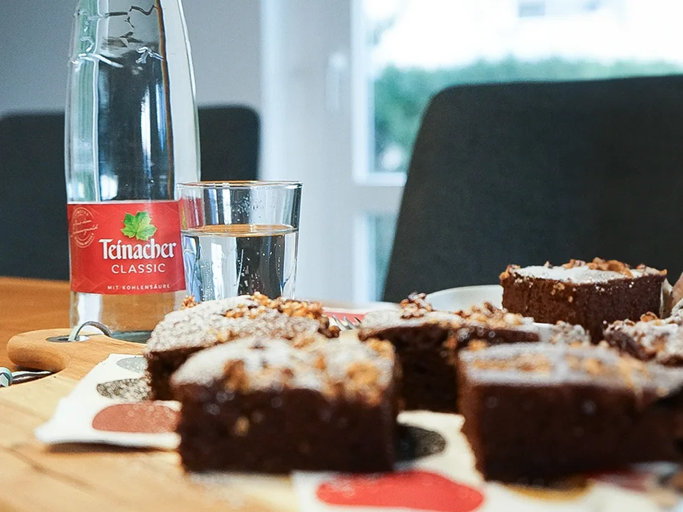 Vorderansicht einem Stück Schokokuchen auf einem Tisch mit einer 0,75 Liter Genussflasche im Hintergrund