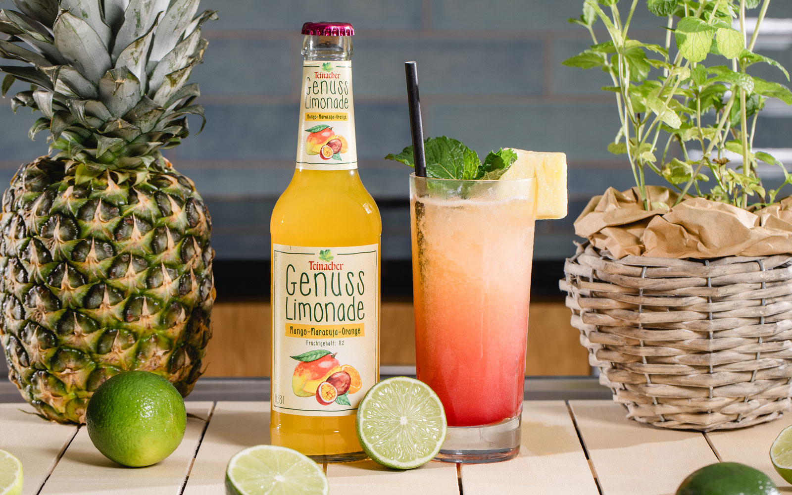 Flasche Teinacher Genuss Limonade Rhabarber-Mirabelle neben einem Glas mit Eis, Rosmarin und Fruchtgarnitur, umgeben von Kräutern und Zitrusfrüchten