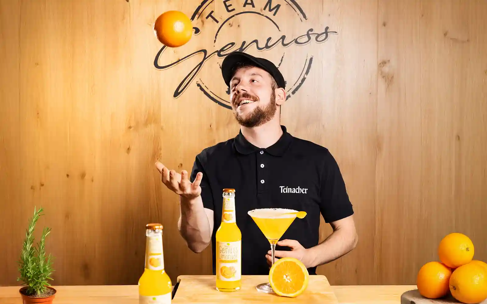 Junger Barkeeper mit Teinacher Limonade jongliert Orange vor Cocktailglas im Team Genuss Studio