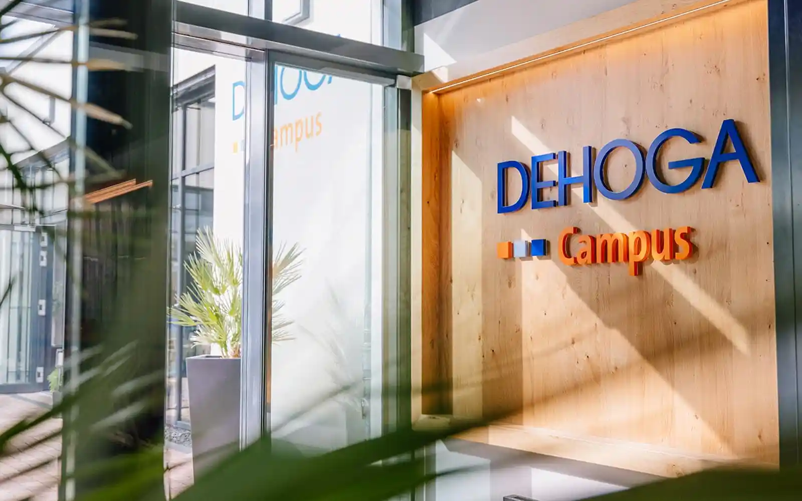 Eingangsbereich des DEHOGA Campus mit Logo an Holztafel und moderner Glasfassade