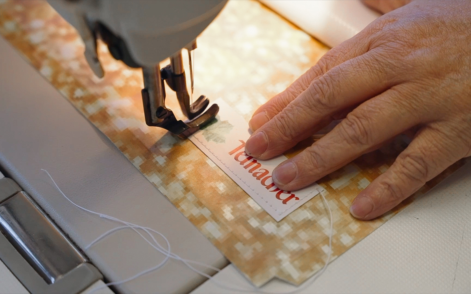 Hände nähen ein Teinacher-Label mit der Nähmaschine auf zugeschnittenes Plakatmaterial zur Fertigung einer Upcycling-Tasche