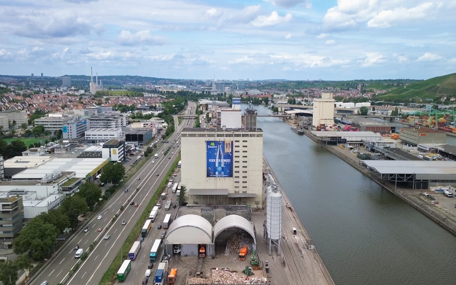 Luftaufnahme eines Industriegebäudes am Neckar mit großem Teinacher-Werbeplakat „10 Jahre Genussflasche“, umgeben von Straße, Hafenanlagen und Stadt