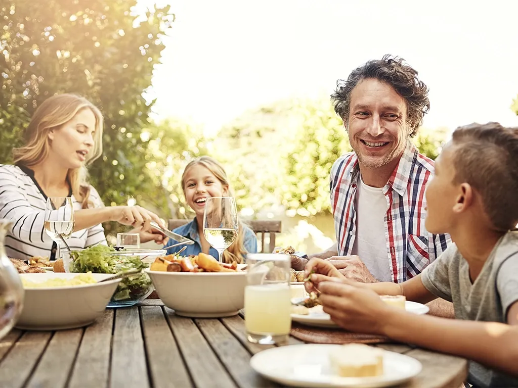 Familie sitzt draußen am Tisch und isst gemeinsam bei Sonnenschein