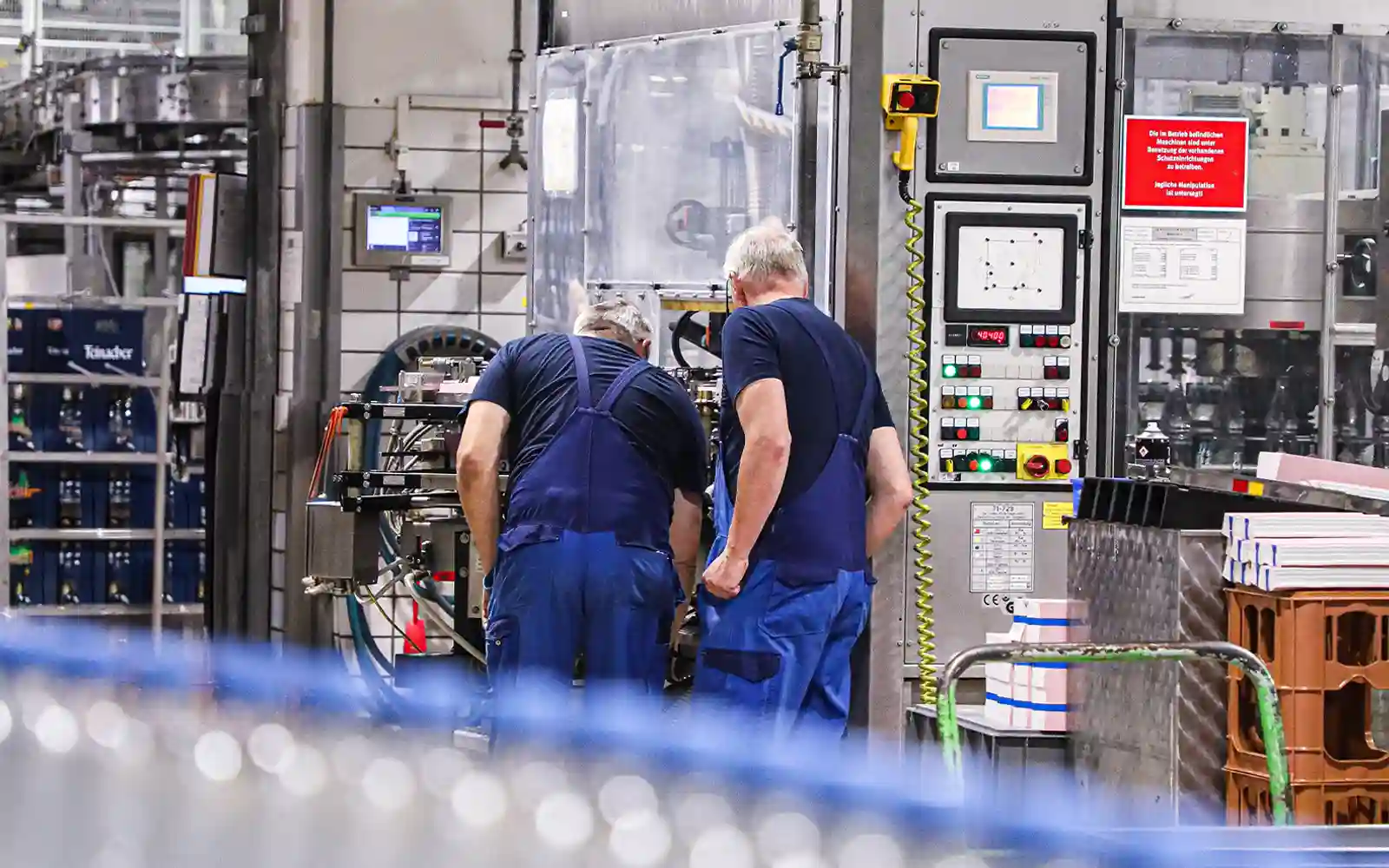 teinacher-wissenswert-nachhaltigkeit-produktion-abfuellanlage Zwei Mitarbeiter in blauer Arbeitskleidung an einer Abfüllanlage in der Teinacher Produktion.