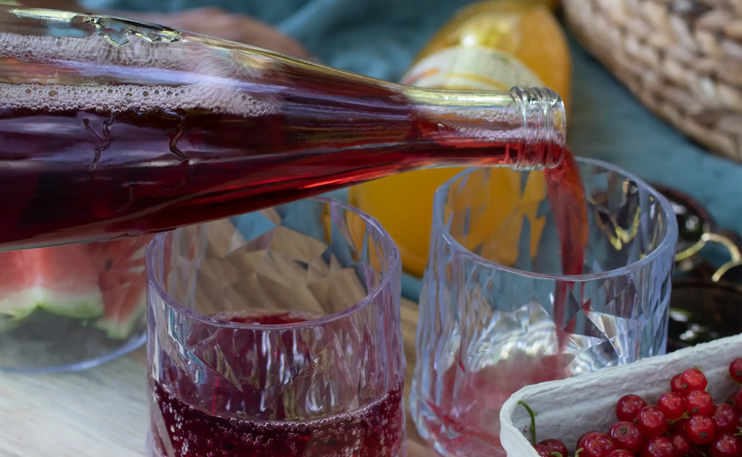 Zwei Gläser in die Teinacher Genuss-Limonade Johannisbeer-Holunder aus der Genussflasche 0,75 L eingeschenkt wird.<br />
