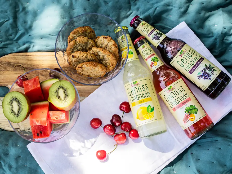 3 Flaschen Limonade mit Obst und Keksen auf Tisch