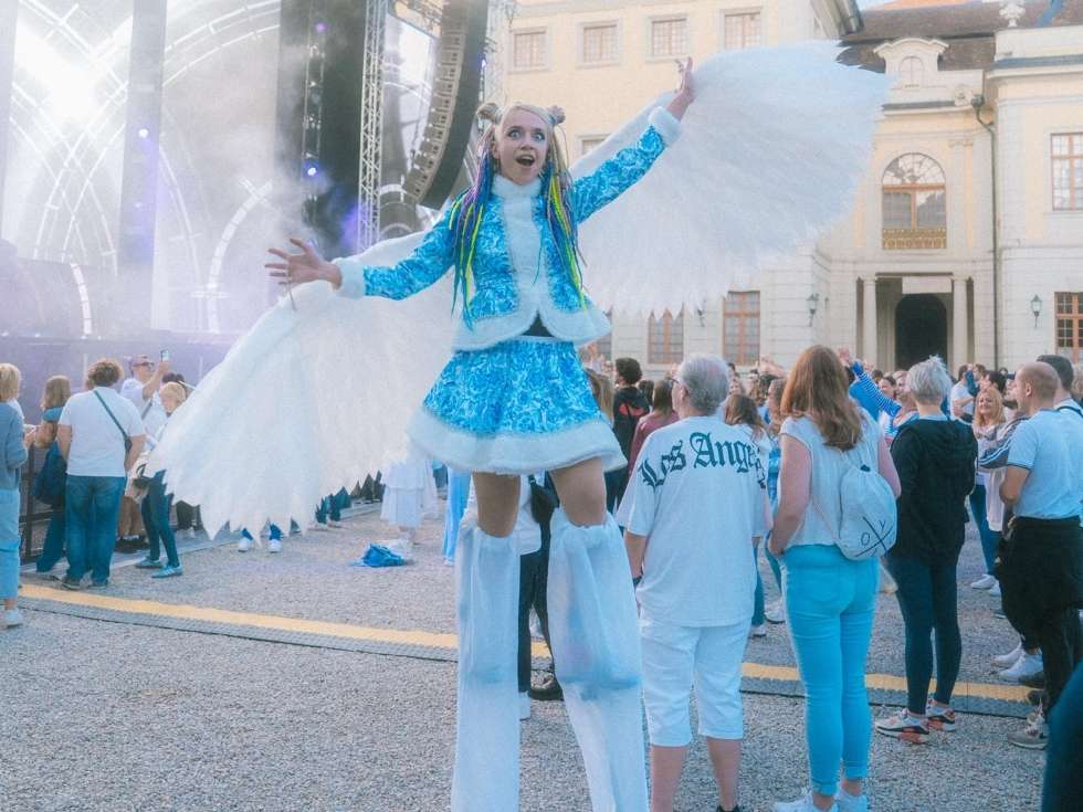 Künstlerin auf Stelzen mit Flügelkostüm beim Event „Just White & Blue“ vor begeistertem Publikum