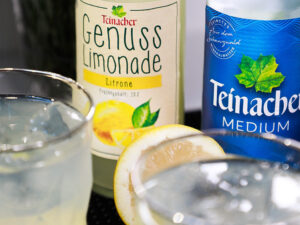 Teinacher Longneck Flaschen mineralwasser Medium und Genuss-Limonade Zitrone mit 2 Gläsern gefüllt mit Eiswürfeln